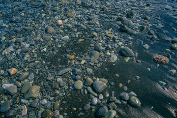 Wet stones scattered across the black volcanic sand shoreline with gentle ocean waves along the coast of Iceland