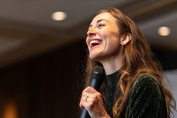 A close-up captures a woman smiling as she passionately speaks during a public speaking event. Her energy engages the audience, showcasing her confidence and charisma