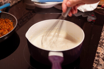 Bechamel sauce simmering in a pan while whisking.