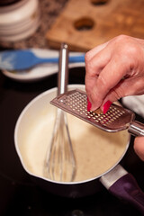 Preparing delicious bechamel sauce in a pan and grating nutmeg.