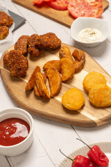 Fried potatos and Fried potatos and nuggets served on a wooden board on a white wooden table. More ingredients surround them: ketchup and mayonnaise, sliced tomatoes and chilli pepper. 45 degree views