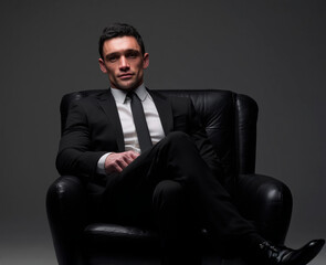 Professional man in formal black suit and tie sitting in leather armchair with confident expression, symbolizing leadership, authority, and success.
