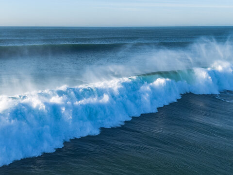 Aerial view of powerful waves crashing with frothy white crests against the deep blue sea at Dixon Park, Newcastle, Australia.