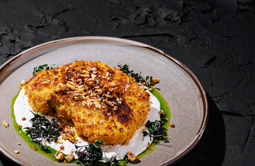 Gourmet breaded cutlet with nuts, microgreens, and sauces on a ceramic plate. Fine dining restaurant dish with creative plating and elegant food presentation.