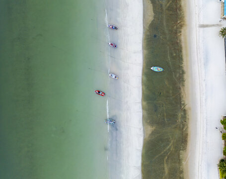 Aerial view of boats resting on the shore where the green sea meets the sandy beach, creating a serene coastal scene, Hua Hin, Prachuap Khiri Khan, Thailand.