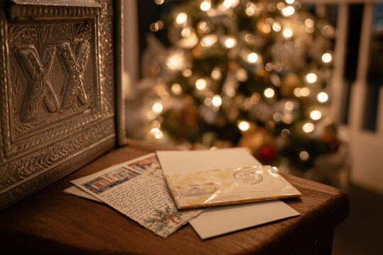 Festive letters and cards rest on a wooden surface, with a sparkling Christmas tree illuminating the background in soft light