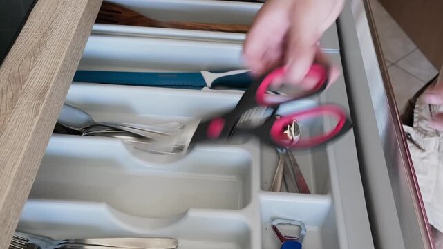 Hand opens kitchen drawer, selects scissors from organized cutlery compartment, then closes it. Clean modern setting with smooth wooden cabinetry and efficient storage solutions.