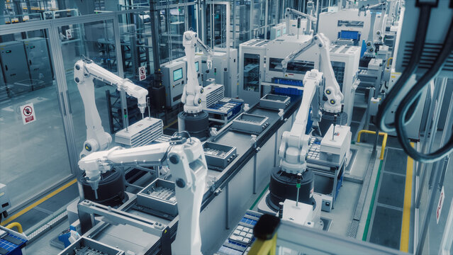 High Tech Factory with White Robotic Arms Assembling Electronic Components on a Production Line Conveyor Belt. Automation and Artificial Intelligence in a Modern Manufacturing Process. High Angle