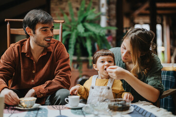 A loving family spending quality time indoors, enjoying breakfast at a nicely set table. The parents with their child share a warm and joyful moment together in a cozy setting.