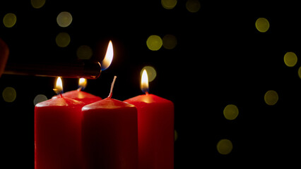 A hand lights a red candle surrounded by soft bokeh lights, creating a warm and cozy atmosphere during the evening.