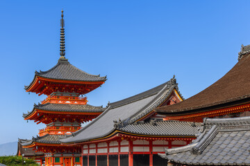 Obraz premium Sanjunoto Pagoda and tiled rooftops at Kiyomizu-dera in Kyoto, Japan, under bright daylight with detailed wooden structures and clean blue sky backdrop