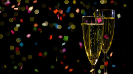 Two flutes of sparkling drink sit amidst colorful confetti, adding to the festive celebration atmosphere.