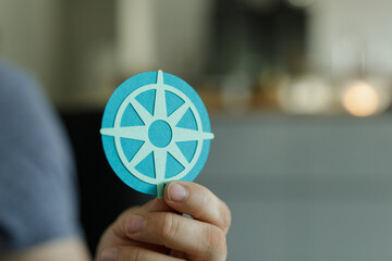 Close-up of a hand holding a teal paper compass.  Guidance, direction, and finding your way.