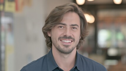 Fototapeta premium Portrait of a Smiling Man with Brown Hair and a Blue Shirt Looking Directly at the Camera with a Blurred Background
