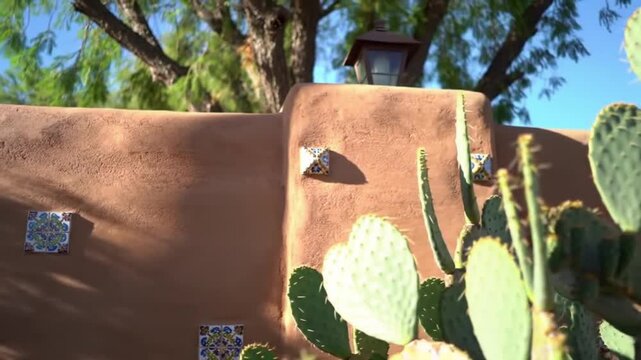 Warm afternoon light bathes a textured adobe wall adorned with decorative tiles and vibrant cacti, evoking a serene Southwestern charm and a sense of timeless tranquility