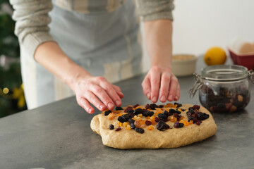 Hand puts dried fruits into brown raw dough in a cozy kitchen in a cozy atmosphere. The baker is preparing a traditional treat, embodying festive spirit and culinary creativity.