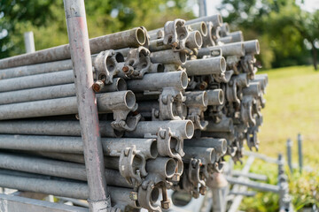 Stack of galvanized steel scaffolding pipes with clamps stored outdoors, construction site equipment prepared for building projects, renovation, structural support and industrial assembly work