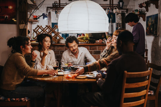 Friends enjoy an intimate meal together in a warmly lit and inviting environment, creating a sense of togetherness and comfort. The scene emphasizes social bonding and relaxed dining moments indoors.