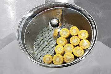 Steamed corn on the stove in a saucepan with a transparent lid.