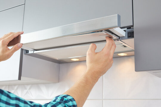 Mans hands removing a filter from cooker hood for cleaning or service. Replacing filter in kitchen hood. Modern kitchen fan or range hood.