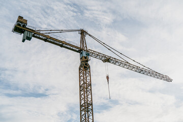 Tower crane with long steel jib and lifting hook against cloudy sky, representing heavy construction machinery, building industry equipment and modern city infrastructure projects