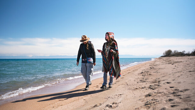 A lesbian couple in love is strolling along the beach. Two best friends spend time together by the lake. The women chat casually