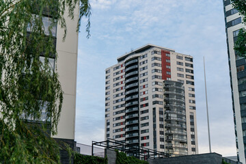 Modern high rise residential apartment tower with glass balconies and red facade details surrounded by urban greenery, representing real estate investment, rental housing and property market growth