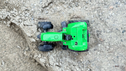 Green toy tractor in sand soil, miniature farming vehicle for children's play, concept of agriculture, childhood imagination, construction toy for kids, rural countryside lifestyle background. High
