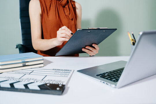 Creative female filmmaker working with tablet, clapperboard, and laptop in modern studio office. Film production, planning, and content creation scene.