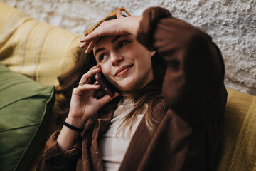 A cheerful woman in a cozy outfit chats on her phone while lounging comfortably.