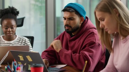 Three concentrated informal business diversity people together team focused indoor in office Indian pensive man with laptop thinking Caucasian female writing notes African American woman with computer - Powered by Adobe