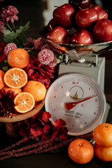 apples and oranges fruit on a scale with colorful flower decorations on a wooden table 