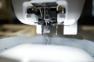 A sewing machine working in a textile factory industrial setting. Metal cotton sewing machine industry. Cotton sewing and fabrication textile industries. Metal hanger rails.