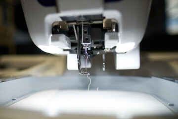 A sewing machine working in a textile factory industrial setting. Metal cotton sewing machine industry. Cotton sewing and fabrication textile industries. Metal hanger rails.