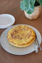 Delicious homemade Spanish omelette or tortilla de patatas, presented on a white plate with a knife and fork aside, ready to be served, perfectly cook traditional dish prepared with potatoes and eggs