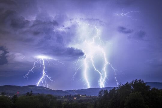 View of electrifying bolts of lightning illuminating the night sky above the rolling hills and trees in a display of raw power, Graz, Styria, Austria.