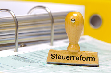 Ein Holzstempel ist beschriftet mit Steuerreform über einem Aktenordner mit Steuerformularen als...