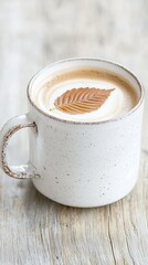 A cozy cup of coffee topped with a delicate leaf design, resting on a rustic wooden surface.