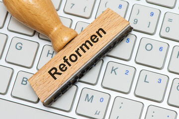 Ein Holzstempel ist beschriftet mit Reformen über einer Computer Tastatur als Symbolbild für...