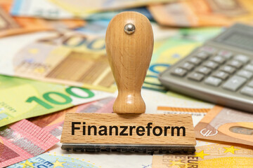 Ein Holzstempel ist beschriftet mit Finanzreform über vielen Euro Banknoten als Symbolbild für...