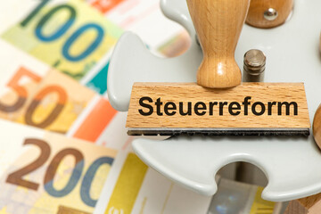 Ein Holzstempel ist beschriftet mit Steuerreform über vielen Euro Banknoten als Symbolbild für...