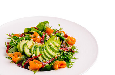 Fresh salad with avocado, smoked salmon, and pine nuts on a white plate