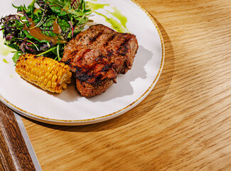 Grilled steak served with fresh salad and corn on wooden table