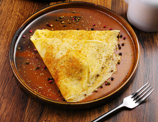 Savory golden crepe served on a brown plate with spices and fork
