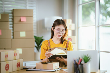 A young Asian woman entrepreneur works at home, preparing packages, managing online orders, checking documents, and organizing her small business.