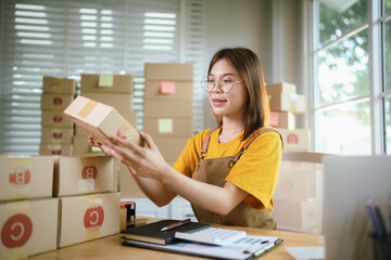 A young Asian female entrepreneur works from home, managing online sales, shipping parcels, marketing products, and ensuring client satisfaction efficiently.