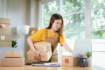 A young Asian female entrepreneur works from home, managing online sales, shipping parcels, marketing products, and ensuring client satisfaction efficiently.