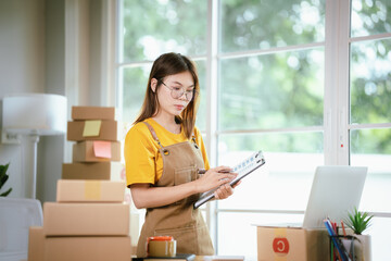 A young Asian female entrepreneur works from home, managing online sales, shipping parcels, marketing products, and ensuring client satisfaction efficiently.