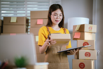 A young Asian female entrepreneur works from home, managing online sales, shipping parcels, marketing products, and ensuring client satisfaction efficiently.