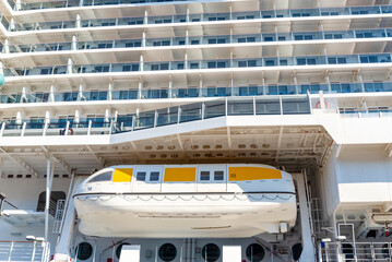 Cruise ship lifeboat stationed at the upper deck in a busy port during bright daylight
